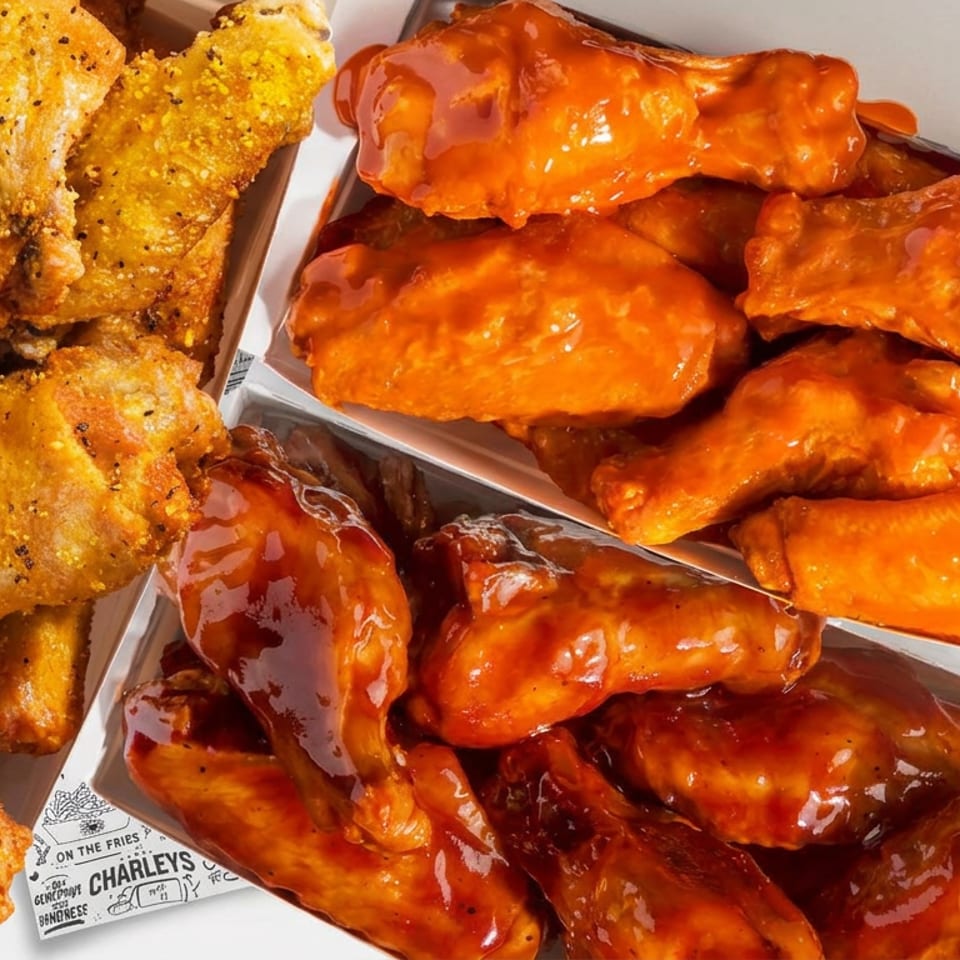 Open takeout boxes filled with golden fried chicken tenders and wings coated in glossy orange and dark barbecue sauces.