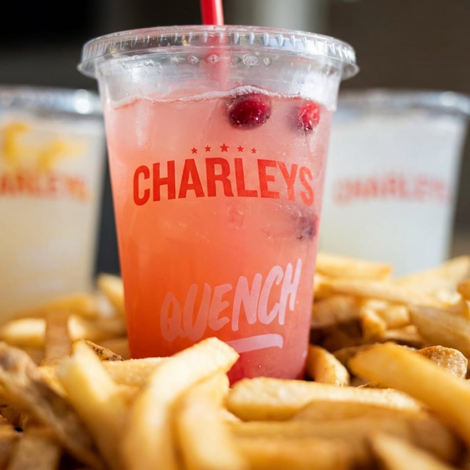 Charleys-branded pink cherry drink with a straw surrounded by piles of golden French fries and grilled chicken strips.